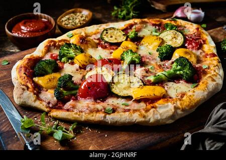 Alto angolo di sana pizza vegetariana fatta in casa servita su tagliere di legno in cucina Foto Stock