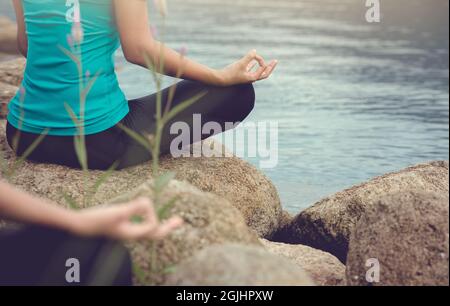 La giovane donna che pratica yoga e medita nella posa del loto all'aperto accanto al lago al mattino. Foto Stock