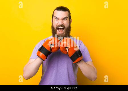 Determinato uomo bearded sta portando alcuni guanti rossi di boxing su sfondo giallo. Foto Stock