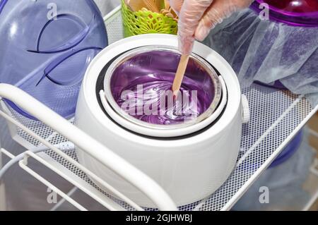 Foto di cera viola fusa su bastone di legno per depilazione Foto Stock