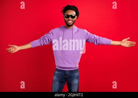 Photo ritratto uomo sorridente indossare occhiali da sole invitanti amici isolato vibrante rosso sfondo di colore Foto Stock