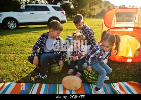 Quattro bambini che trascorrono il tempo insieme. Coperta per picnic all'aperto, seduta con cocomeri. Foto Stock