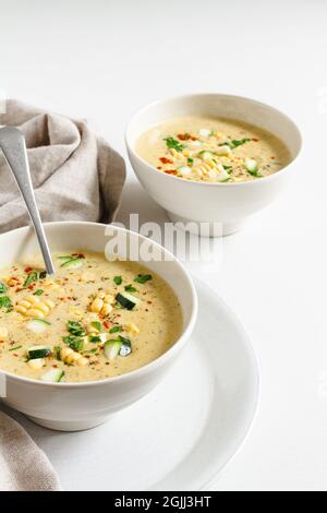 Due ciotole di mais cremoso e zuppa di zucchine condite con prezzemolo e pepe di cayenna. Foto Stock