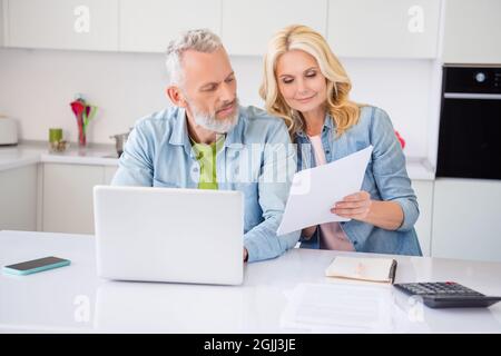 Foto di coppia pensieroso piuttosto vecchio indossare denim camicia sorridente lettura dicuments navigazione dispositivo moderno interno casa camera Foto Stock