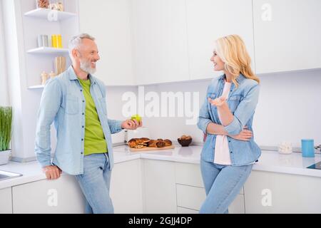Foto di dolce affascinante coppia invecchiata indossare jeans camicia sorridente in piedi comunicante casa camera interna Foto Stock