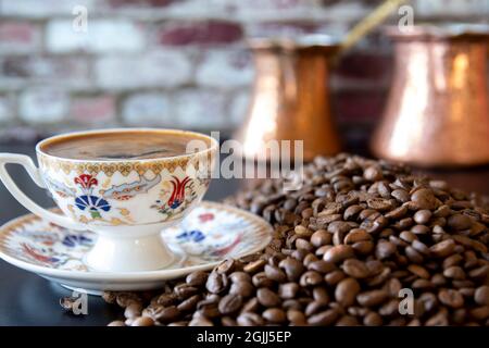 Caffè turco su una tazza di fumo, fagioli accanto e pentole sullo sfondo. Focus Cup selettivo. Foto Stock