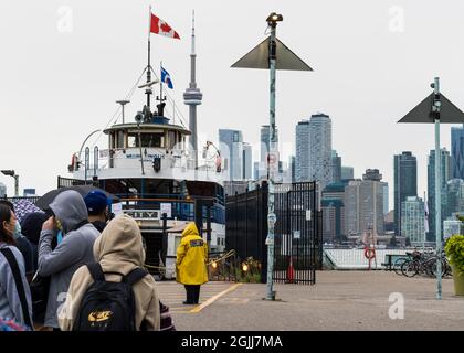 Toronto, Ontario, Canada - Luglio 31 2021: Retro-vista selettiva focus sulla guardia di sicurezza donna in gialle giacca di fronte a un traghetto sul molo delle Isole Toronto. Foto Stock