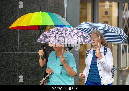 Tre donne con ombrelloni multicolore in una giornata di pioggia a Preston, Lancashire. Meteo Regno Unito 10 settembre 2021. Negozi, negozi, shopping in una giornata di esposizioni nel centro di Preston. Credit; MediaWorldImages/AlamyLiveNews Foto Stock