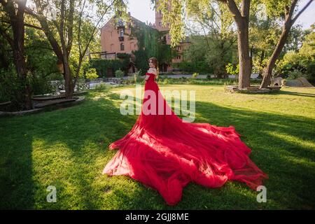 Bella donna tattoed rosso in lungo vestito rosso che posa vicino al castello Foto Stock