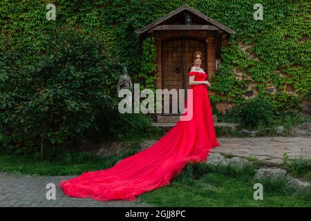Bella donna tattoed rosso in lungo vestito rosso che posa vicino al castello Foto Stock