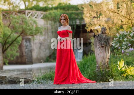 Bella donna tattoed rosso in lungo vestito rosso che posa vicino al castello Foto Stock