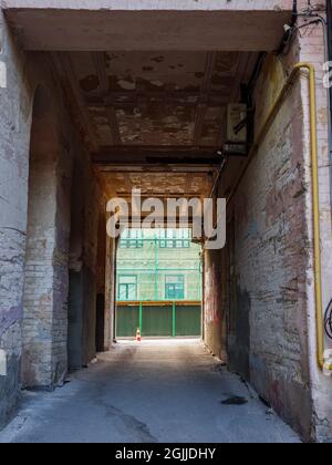 Arco attraverso l'antico edificio in mattoni a tempo con vista sull'edificio in mattoni a due piani a due piani in muratura abbandonato nel centro della città di Kyiv. Foto Stock