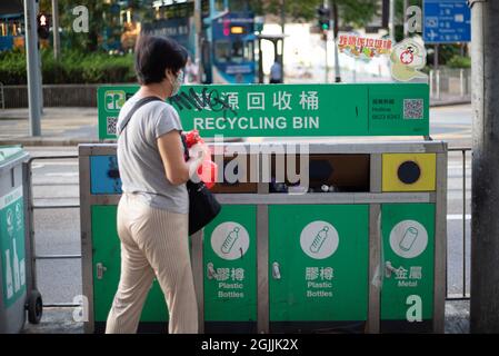 10 9 2021 bidoni classificati per rifiuti di carta, bottiglie di plastica e lattine metalliche a Hong Kong, con una donna getta rifiuti in bidoni. Foto Stock