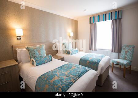 Semplice camera interna con due letti singoli, cuscini turchesi e una sedia Foto Stock