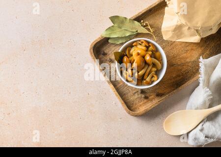 Funghi di miele sottaceto serviti in ciotola con foglia di alloro e spezie su sfondo beige. Vista dall'alto. Spazio di copia. Foto Stock