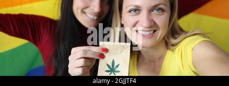 Due donne sorridenti che tengono bandiera lgbt e pacchetto di marijuana Foto Stock