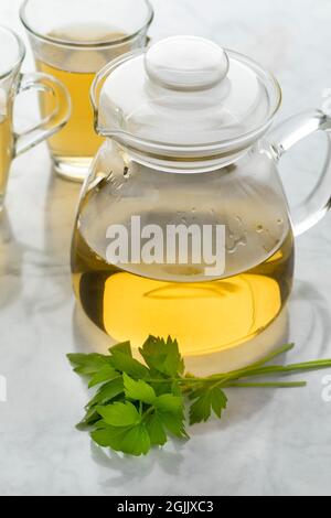 Teiera di vetro con tè di lovage e un rametto di lovage fresco di fronte Foto Stock