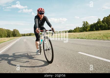 Giovane donna in casco seduta su una bicicletta e in bicicletta all'aperto Foto Stock