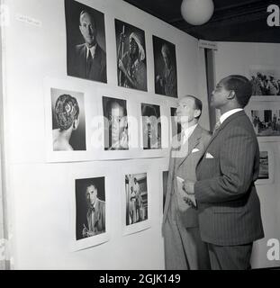 Anni '50, storico, in una mostra fotografica, due uomini in tuta in piedi guardando i ritratti dall'Africa e la Gold Coast, preso dal fotografo Leslle J. Taylor, AIBP, Londra, Inghilterra, Regno Unito. Foto Stock