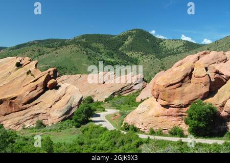 Colorado paesaggio estivo al Red Rocks Park con strada tra formazioni geologiche di arenaria e verdi colline e vegetazione lussureggiante Foto Stock