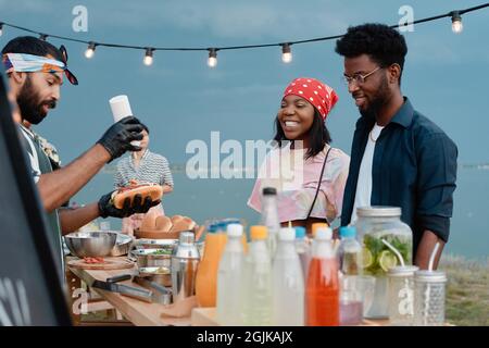 Giovane coppia africana che guarda per il processo di preparazione hot dog che hanno pranzo sulla spiaggia all'aperto Foto Stock