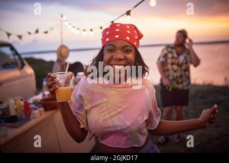 Ritratto di donna felice Africana con bevanda alcolica sorridente alla macchina fotografica mentre balla al Beach party Foto Stock