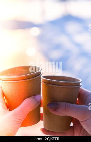 Mano di donne con tazza di carta di caffè in fondo neve invernale. Tazze monouso in carta marrone scuro. Caffè da portare via. Pausa caffè Foto Stock