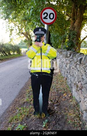 Cartoncino cut-out falso agente di polizia stradale con pistola di velocità attaccato al segnale limite di velocità 20 mph, Fortinghall, Perth e Kinross, Scozia, Regno Unito Foto Stock