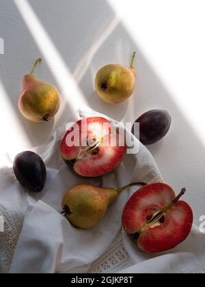 Appartamento autunnale posato con mele rosse fresche Pere su tela bianca da tavola in lino su sfondo chiaro con ombre dure. Vacanze di ringraziamento cibo sano Foto Stock
