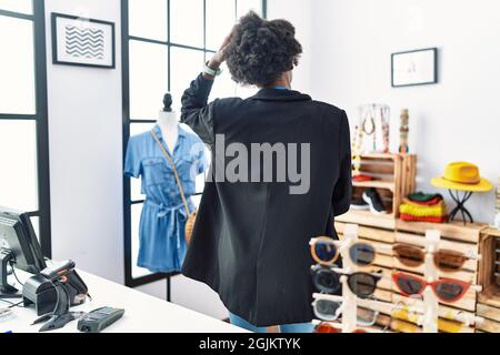 Giovane donna africana che lavora come manager al negozio boutique indietro pensando al dubbio con mano a testa Foto Stock