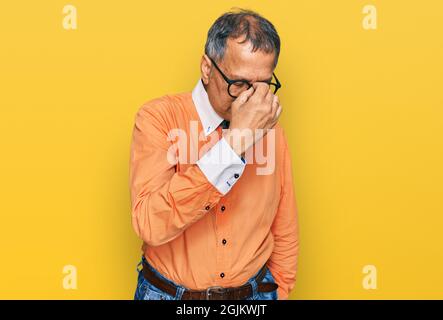 Uomo indiano di mezza età che indossa abiti e occhiali casual stanco sfregare naso e occhi sensazione di affaticamento e mal di testa. Concetto di stress e frustrazione. Foto Stock