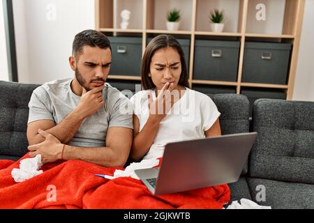 Giovane coppia malata latina che ha teleconsulto medico usando il laptop a casa. Foto Stock