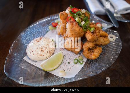 Calamari croccanti guarniti con insalata servita con un bagno di maionese su un piatto di vetro e tavolo di legno. Foto Stock