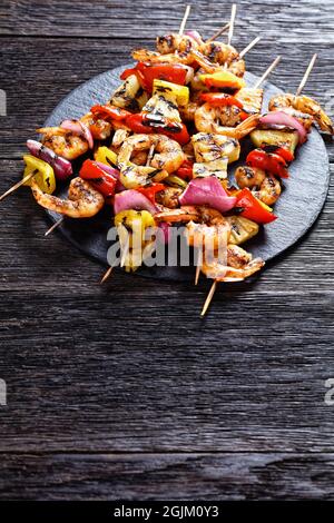 Gamberi Kabobs alla griglia con cipolla rossa, pepe dolce e ananas su un piatto di pietra nera, vista verticale Foto Stock