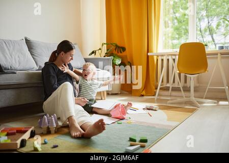 Ragazzo caucasico emozionale carino seduto con carta sulle ginocchia e braccia stretching mentre racconta la storia alla madre a casa Foto Stock
