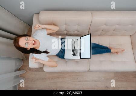Una donna irritata seduta sul divano con un computer portatile. Foto Stock