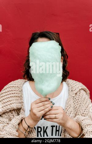 Immagine verticale di una ragazza irriconoscibile che copre il viso con un po 'di zucchero verde, indossa un maglione leggero fatto a mano e dipinge le unghie verde. COP Foto Stock