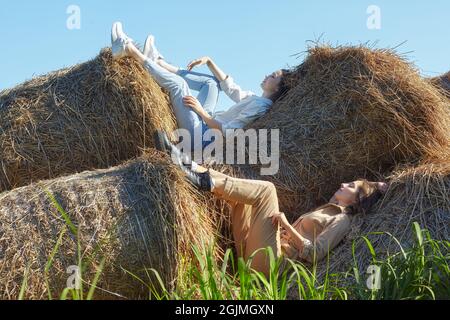 Due giovani donne bruna e bionda giacciono sui rotoli di fieno. Romantiche ragazze di campagna sul fieno. Foto Stock