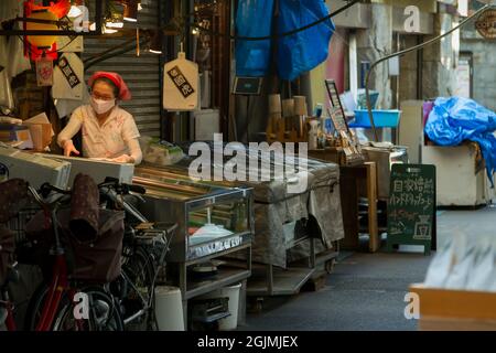 Una donna che lavora al banco di un piccolo negozio di pesce a Tsukiji mercato esterno Tokyo, Giappone Foto Stock