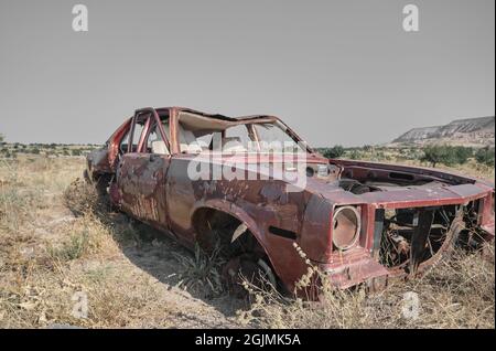 Abbandonata e brunnfield auto in stile vintage in piedi su campo agricolo coperto da piante gialle e erba Foto Stock