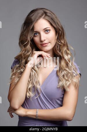 Studio ritratto di bellezza di una giovane donna in un abito estivo. Donna bionda in abito estivo su sfondo grigio. Ragazza con mano vicino alla faccia. Foto Stock