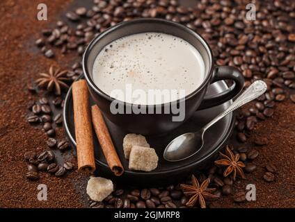 Tazza di cappuccino in ceramica con cannella e zucchero di canna con stella all'anice e cucchiaio d'argento su fondo di caffè macinato e fagioli. Foto Stock