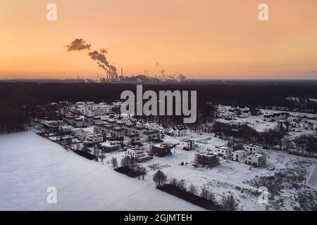 Immagine drone da una zona residenziale coperta di neve e fabbrica industriale durante il tramonto in Germania Foto Stock