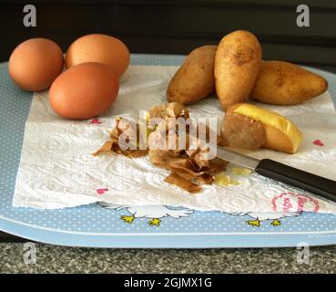 Primo piano delle preparazioni per un'insalata di patate, con la buccia di patate e il coltello in primo piano, così come più patate e tre uova sbucciate. Foto Stock