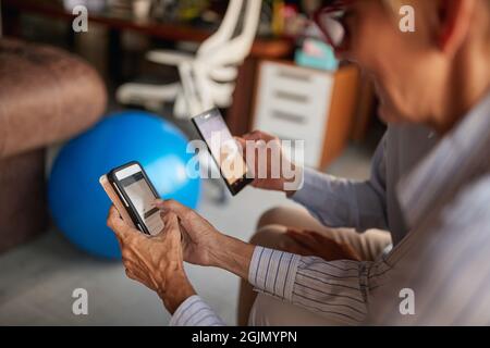 Le donne anziane che usano gli smartphone fanno una pausa in un'atmosfera rilassata sul posto di lavoro. Lavoro, ufficio, lavoro Foto Stock