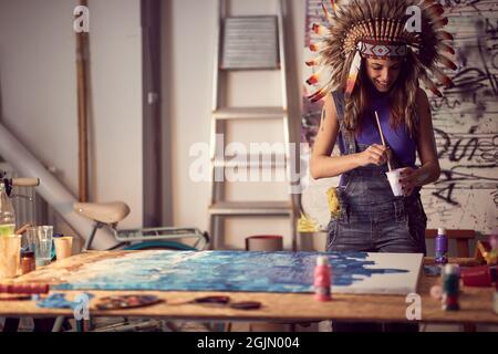 Una giovane artista femminile con un cofano da guerra in un'atmosfera piacevole nello studio è focalizzata su un lavoro su un nuovo dipinto. Arte, pittura, studio Foto Stock