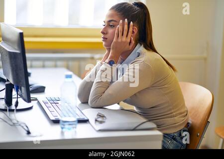 Una studentessa di cattivo umore per una nuova difficile lezione di informatica nella classe universitaria. I giovani intelligenti studiano all'università. Istruzione Foto Stock