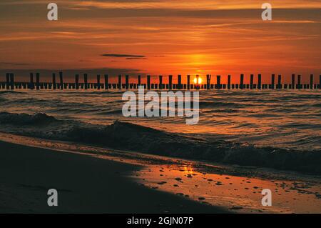 Tramonto a Zingst al mare. Il sole rosso arancio tramonta all'orizzonte. I gabbiani girano nel cielo. Una bella atmosfera luminosa che vi invita a sognare. T Foto Stock