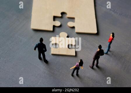 Lavoro di squadra aziendale con puzzle finishing progetto di cooperazione Unity concetto. La gente in miniatura guarda il puzzle mancante Foto Stock