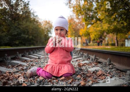 cute toddler ragazza che gioca con pietre sul terrapieno ferroviario. giochi pericolosi Foto Stock